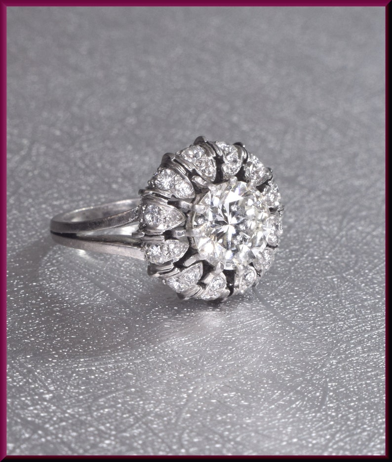 May include: A silver ring with a large, round, clear diamond surrounded by smaller diamonds in a flower-like design.