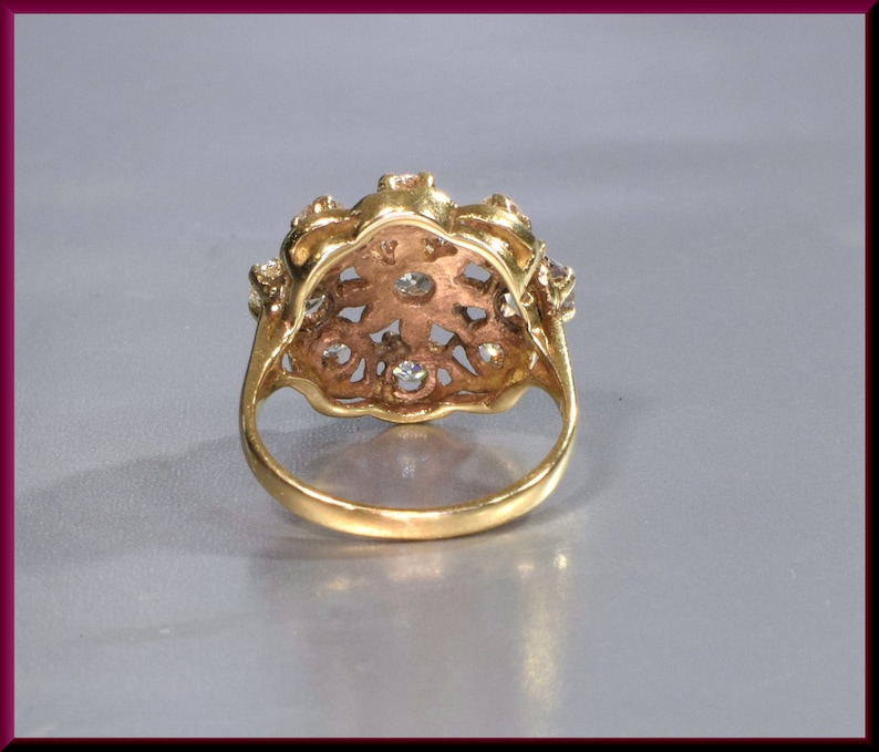 May include: A gold ring with a floral design and clear stones. The ring is set with a cluster of small stones in the center and smaller stones around the edges.