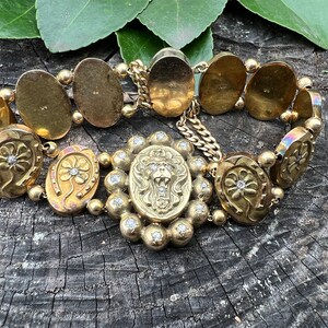 Op de afbeelding: Een gouden armband met een leeuwenkopbedel en hoefijzerbedels met diamanten. De armband is gemaakt van meerdere ovale schakels.