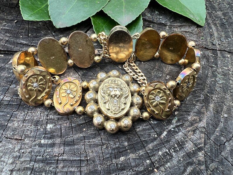 Op de afbeelding: Een gouden armband met een leeuwenkopbedel en hoefijzerbedels met diamanten. De armband is gemaakt van meerdere ovale schakels.