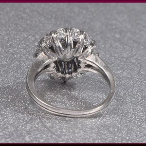May include: A silver ring with a large, round, diamond-encrusted center stone. The ring is set with smaller diamonds around the center stone, creating a halo effect.
