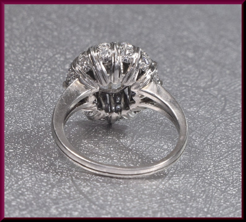May include: A silver ring with a large, round, diamond-encrusted center stone. The ring is set with smaller diamonds around the center stone, creating a halo effect.
