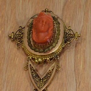 May include: A gold filigree brooch with a cameo of a woman's face carved from red coral.