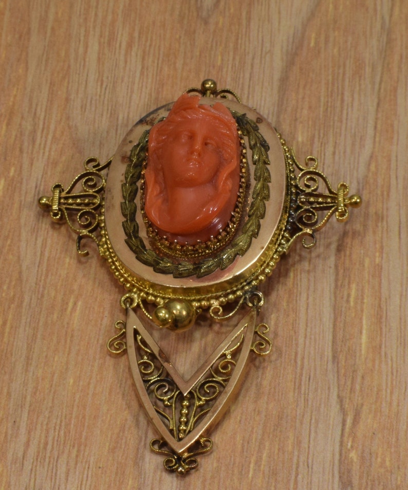 May include: A gold filigree brooch with a cameo of a woman's face carved from red coral.