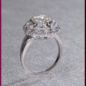 May include: A silver ring with a large, round, clear diamond surrounded by smaller diamonds. The ring has a delicate band.