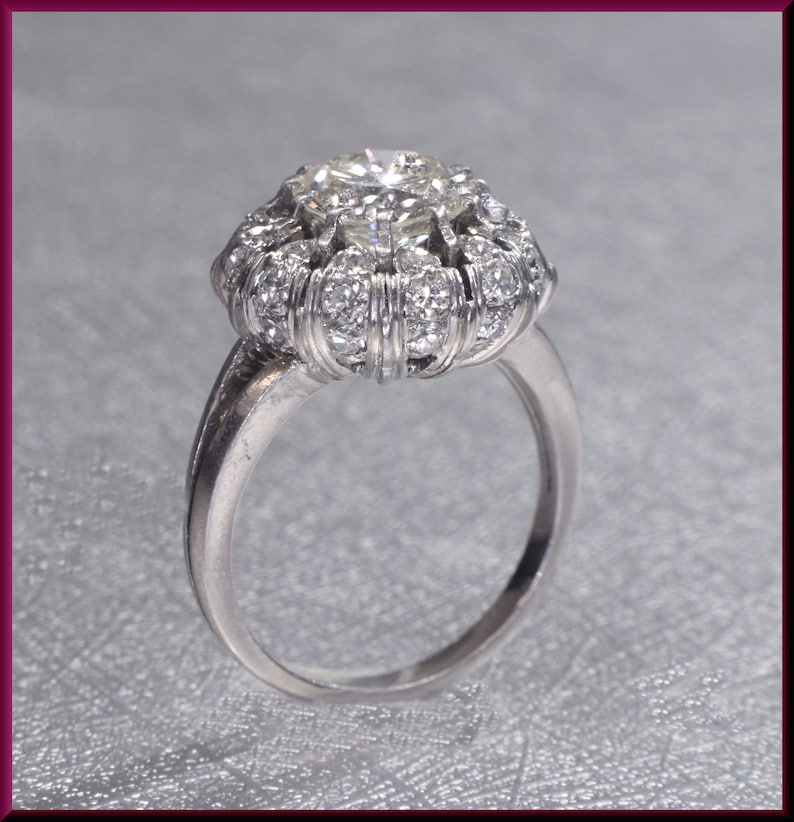 May include: A silver ring with a large, round, clear diamond surrounded by smaller diamonds. The ring has a delicate band.