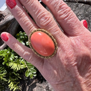 May include: A large oval coral ring with a gold setting. The coral is a vibrant orange colour and the setting is a twisted rope design.