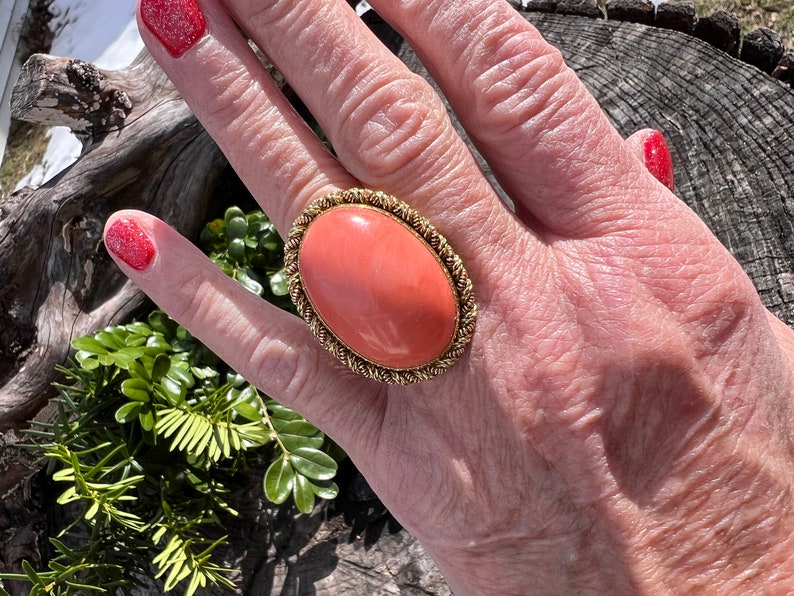 May include: A large oval coral ring with a gold setting. The coral is a vibrant orange colour and the setting is a twisted rope design.