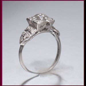 May include: A silver engagement ring with a large, round, clear diamond set in a prong setting. The band is decorated with smaller diamonds.