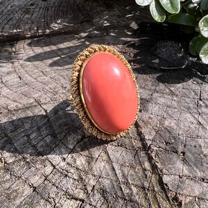 May include: A coral ring with a gold setting. The ring is oval shaped and the coral is a vibrant orange colour.