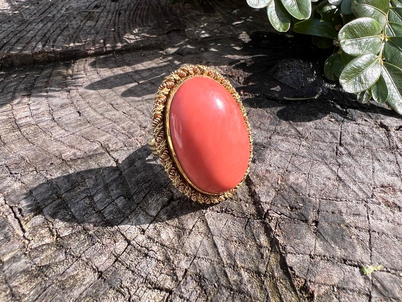 May include: A coral ring with a gold setting. The ring is oval shaped and the coral is a vibrant orange colour.