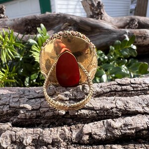 May include: A gold ring with a red stone set in the centre. The ring is made of twisted wire and has a decorative design.