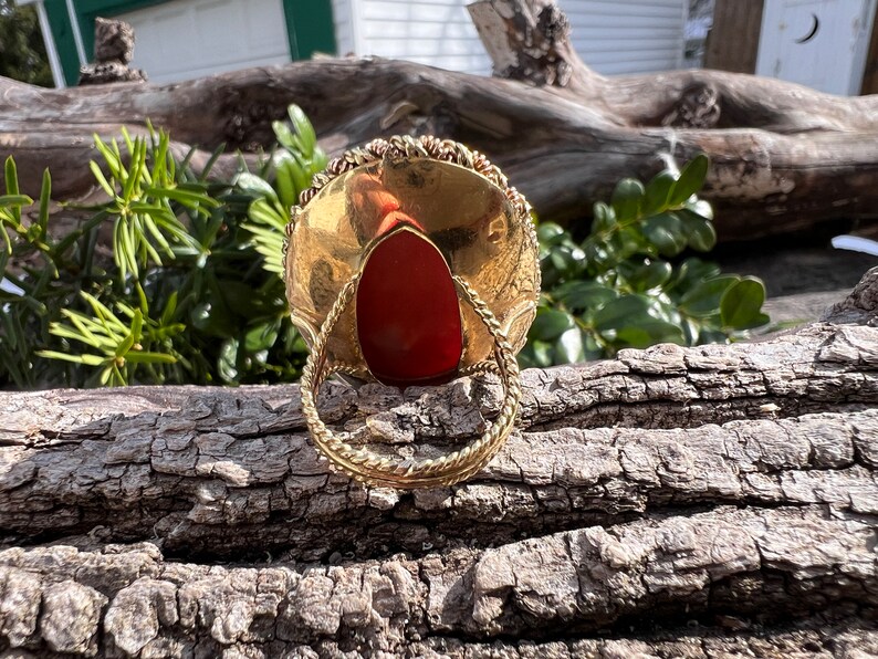 May include: A gold ring with a red stone set in the centre. The ring is made of twisted wire and has a decorative design.