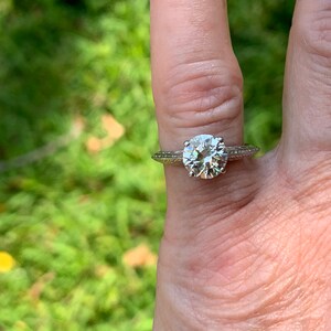 May include: A silver engagement ring with a large, round, clear diamond. The ring has a delicate, textured band.