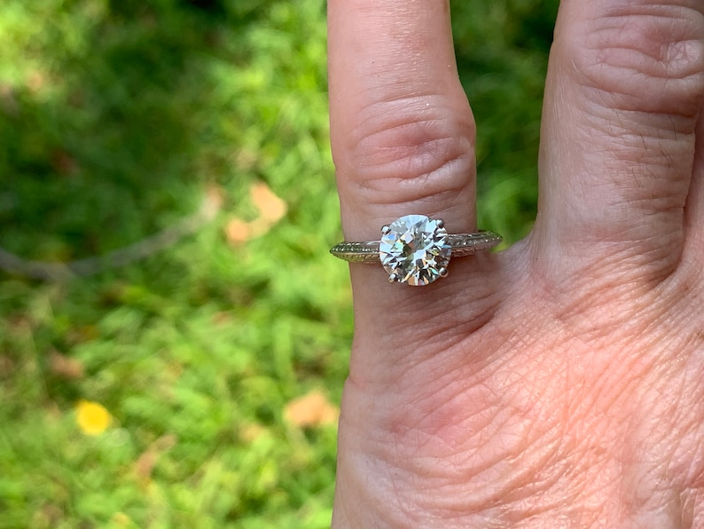 May include: A silver engagement ring with a large, round, clear diamond. The ring has a delicate, textured band.