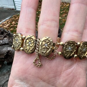 Op de afbeelding: Een gouden armband met een ketting en hoefijzervormige bedels, elk met een klein diamantje in het midden.