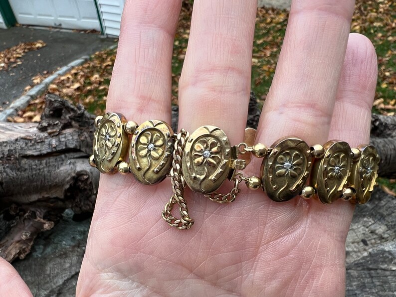 Op de afbeelding: Een gouden armband met een ketting en hoefijzervormige bedels, elk met een klein diamantje in het midden.
