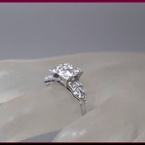 May include: A silver ring with a large square-shaped diamond surrounded by smaller diamonds. The ring is set on a white background.