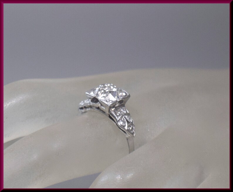 May include: A silver ring with a large square-shaped diamond surrounded by smaller diamonds. The ring is set on a white background.