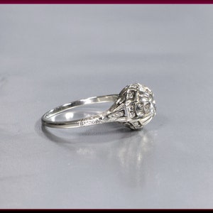 May include: A silver ring with a large, round, clear diamond set in a filigree design. The ring is set on a gray background.