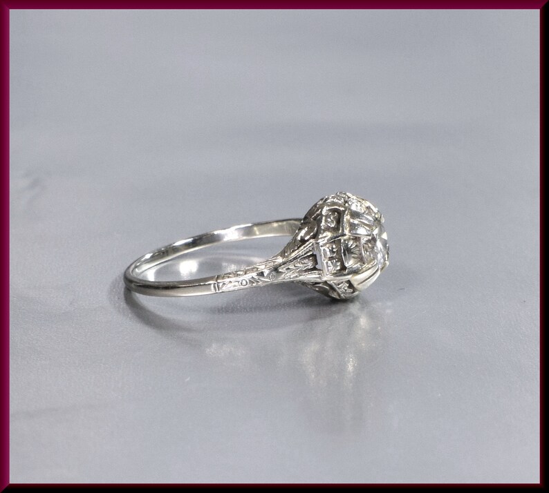 May include: A silver ring with a large, round, clear diamond set in a filigree design. The ring is set on a gray background.