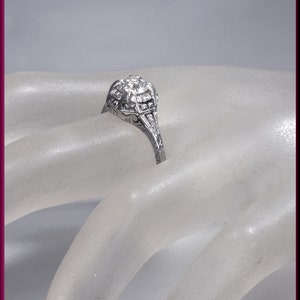 May include: A silver ring with a large, round, clear stone surrounded by smaller stones. The ring has a delicate, intricate design.