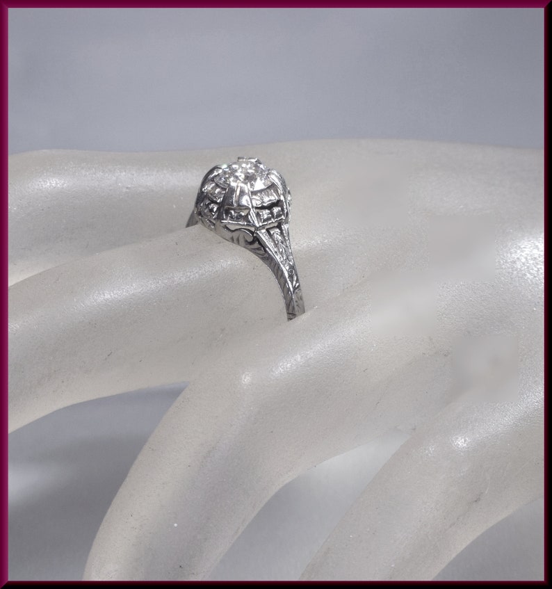 May include: A silver ring with a large, round, clear stone surrounded by smaller stones. The ring has a delicate, intricate design.