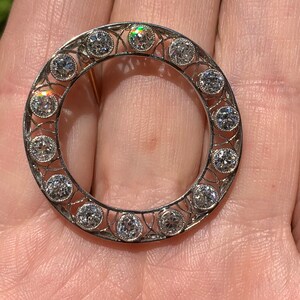 May include: A silver circular brooch with a delicate filigree design and a row of round diamonds around the edge.