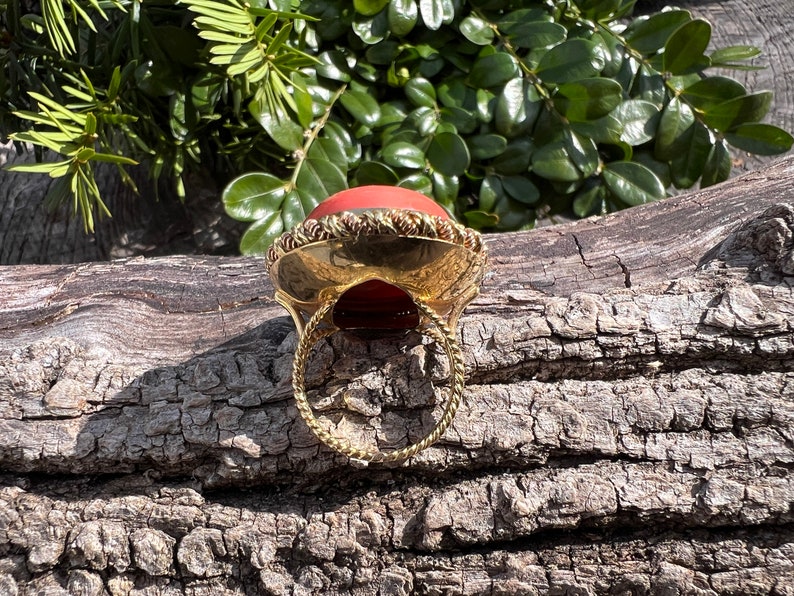 May include: A gold ring with a large, round, red gemstone set in a gold bezel. The ring is on a wooden surface.