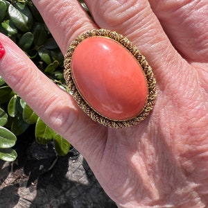 May include: A large oval coral ring with a gold setting. The coral is a vibrant orange colour and the setting is a twisted rope design.