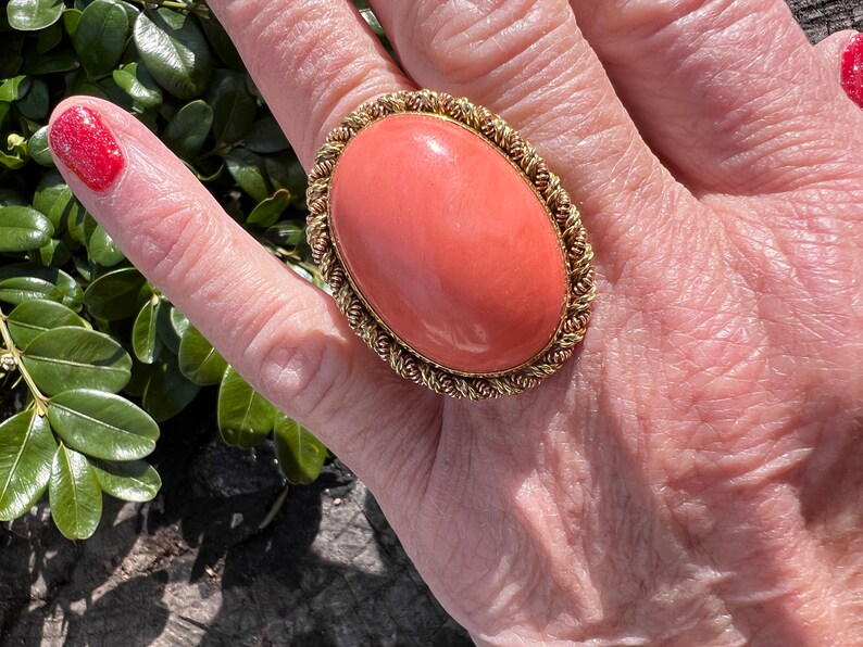 May include: A large oval coral ring with a gold setting. The coral is a vibrant orange colour and the setting is a twisted rope design.