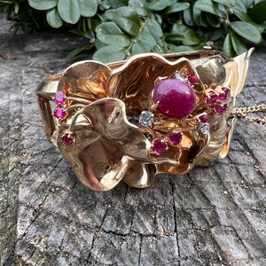 以下が含まれることがあります： 赤い宝石とダイヤモンドが散りばめられた、花柄の金製のブレスレット。