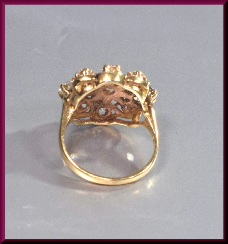 May include: A gold ring with a floral design and clear stones. The ring is set with a cluster of stones in the center and smaller stones around the band.