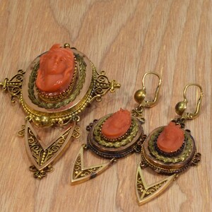 May include: A set of antique coral cameo jewelry featuring a gold filigree design. The set includes a pendant and a pair of earrings.