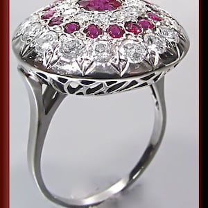 Puede incluir: Un anillo de plata con un gran rubí rojo redondo y un grupo de diamantes engastados en un diseño de filigrana.