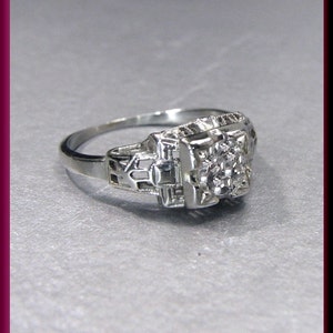 May include: A silver ring with a delicate filigree design and a small, round diamond in the centre.