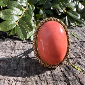 May include: A large, oval-shaped coral ring with a gold setting. The coral is a vibrant orange-red colour and the setting is a delicate, twisted wire design.