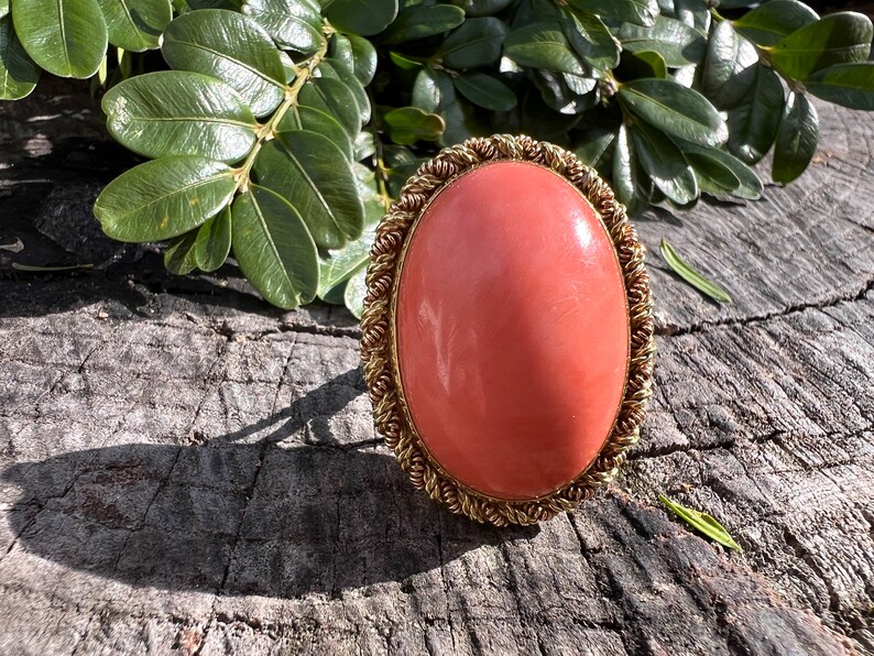 May include: A large, oval-shaped coral ring with a gold setting. The coral is a vibrant orange-red colour and the setting is a delicate, twisted wire design.