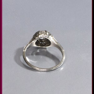 May include: A silver ring with a round, clear stone set in a filigree design. The ring is on a gray background.