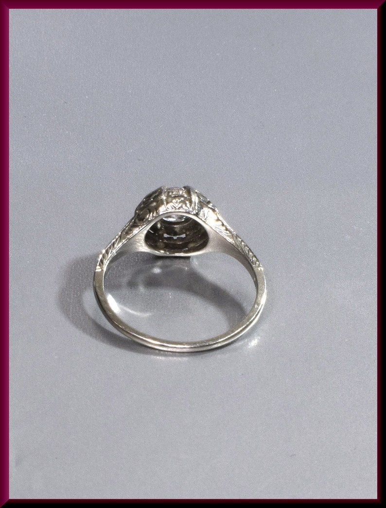 May include: A silver ring with a round, clear stone set in a filigree design. The ring is on a gray background.