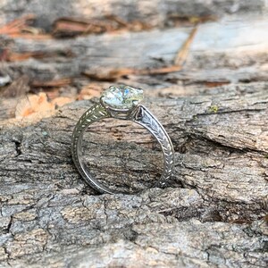 May include: A silver engagement ring with a round, clear diamond set in a delicate, engraved band.
