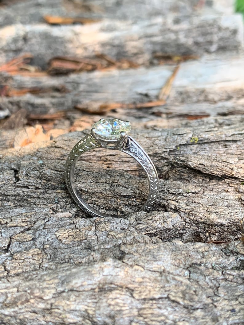 May include: A silver engagement ring with a round, clear diamond set in a delicate, engraved band.