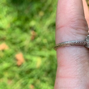 May include: A silver engagement ring with a round diamond set in a simple band. The band has a delicate, engraved design.