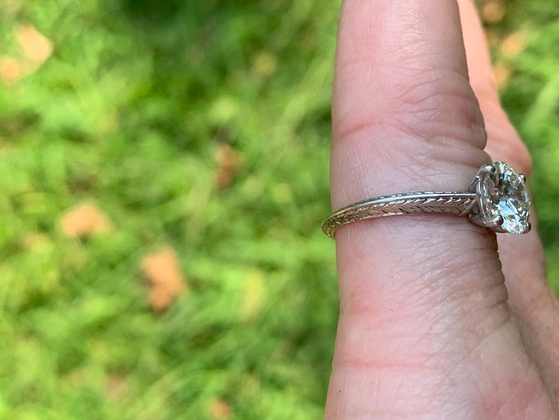 May include: A silver engagement ring with a round diamond set in a simple band. The band has a delicate, engraved design.