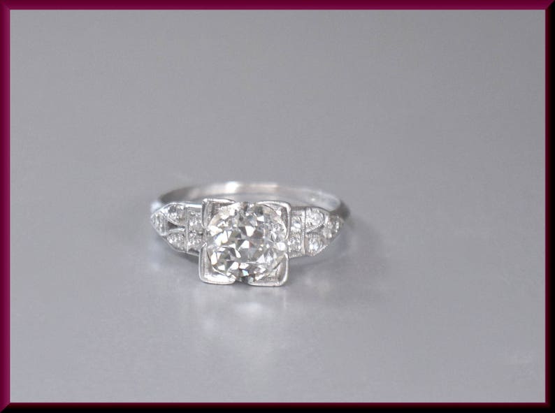 May include: A silver engagement ring with a round, clear diamond center stone and smaller diamonds set in the band.