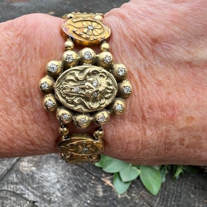 Op de afbeelding: Een gouden armband met een bloemmotief en een leeuwenkop. De armband is versierd met kleine diamanten.