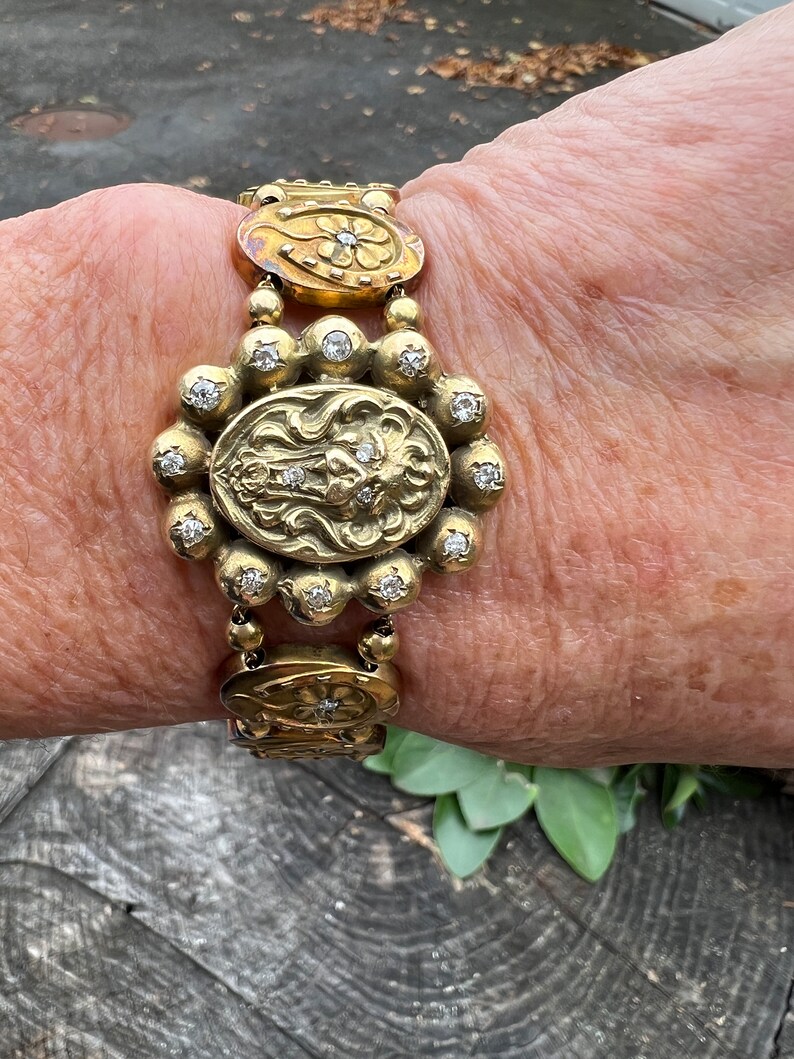 Op de afbeelding: Een gouden armband met een bloemmotief en een leeuwenkop. De armband is versierd met kleine diamanten.