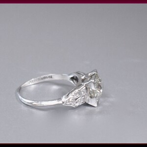 May include: A silver ring with a large, clear diamond center stone and smaller diamonds on the band. The ring is set in a prong setting.