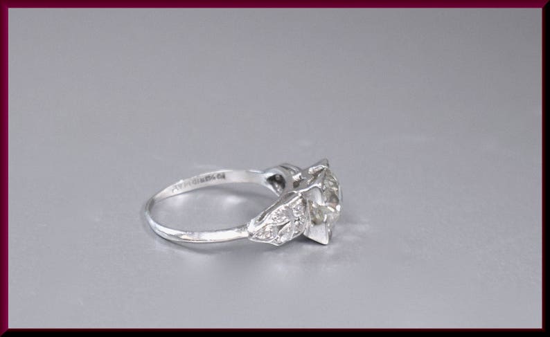 May include: A silver ring with a large, clear diamond center stone and smaller diamonds on the band. The ring is set in a prong setting.