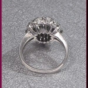 May include: A silver ring with a large, round, diamond-encrusted setting. The ring is set on a gray textured surface.